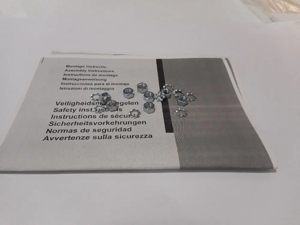Ersatzteile von Remeha, bestehend aus mehreren silbernen Schrauben unter Montageanleitungen in mehreren Sprachen, die auf einem weißen Untergrund liegen.